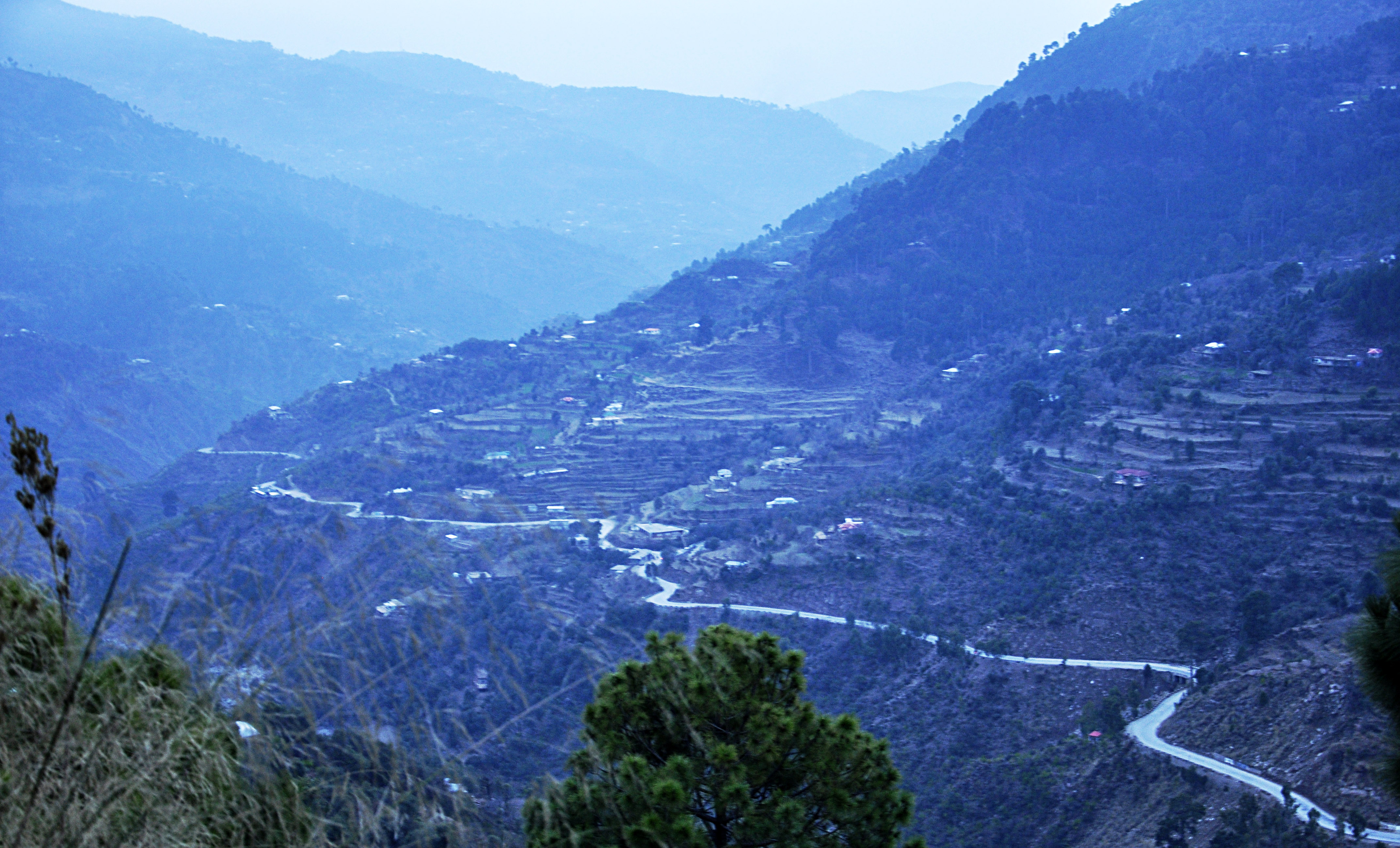 Terraced hillsides and a winding road in the Rawalakot area of Azad Jammu and Kashmir at dusk.