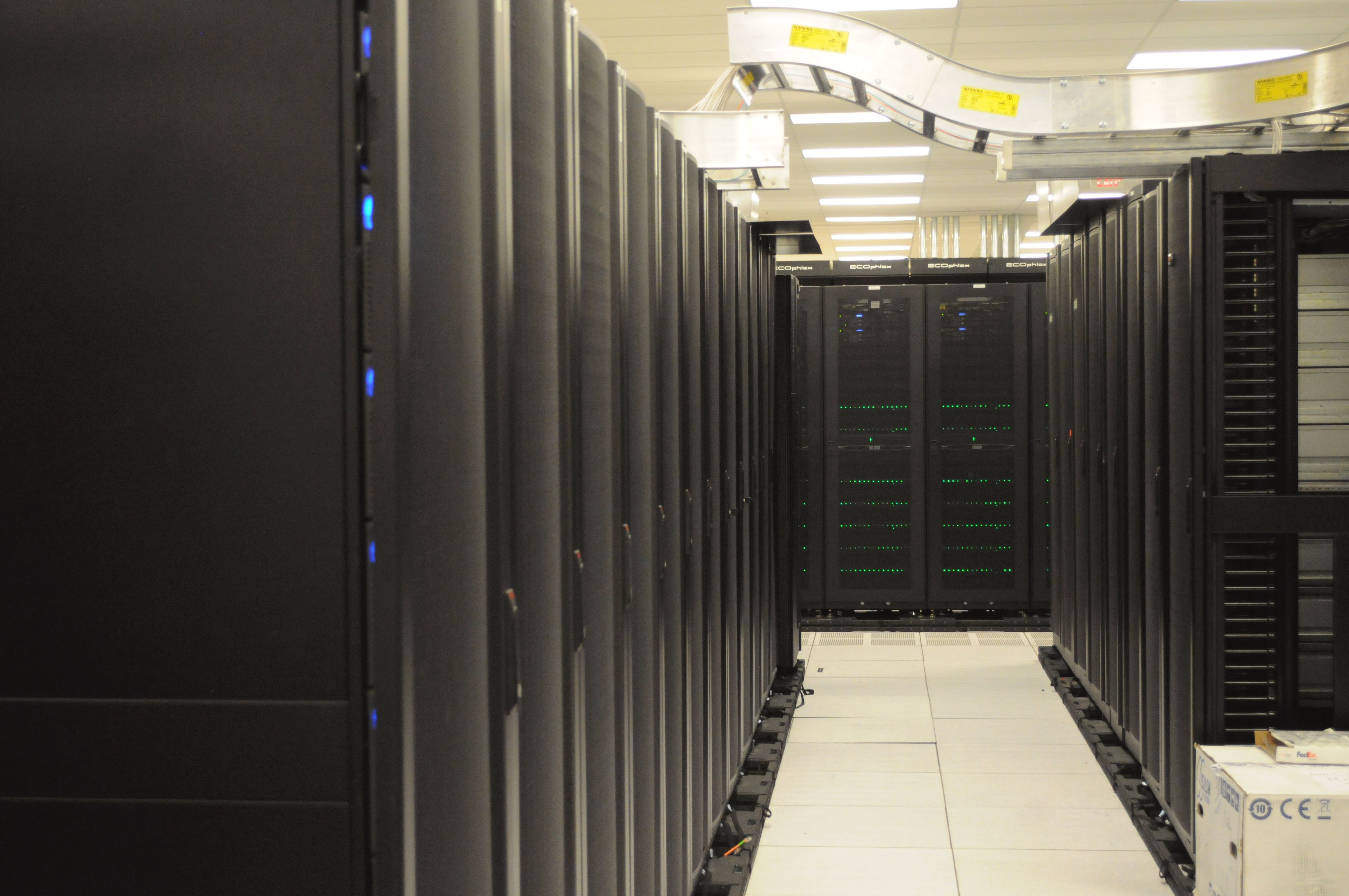 Rows of black server cabinets beneath bundled overhead cables in a computing facility