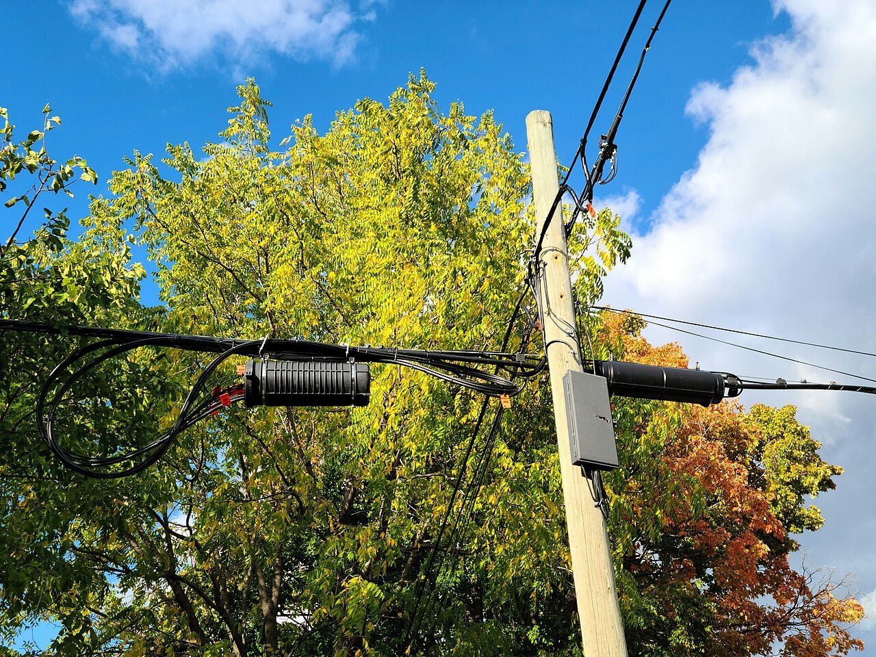 An assortment of communication cables on a surface, including an orange-tagged optical fibre line, bundled copper telephone wires and a coaxial cable.