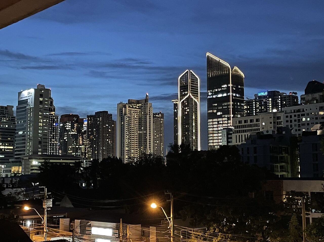 The Sukhumvit skyline in Bangkok, showing residential and commercial towers stretching along the tree-lined boulevard at dusk.