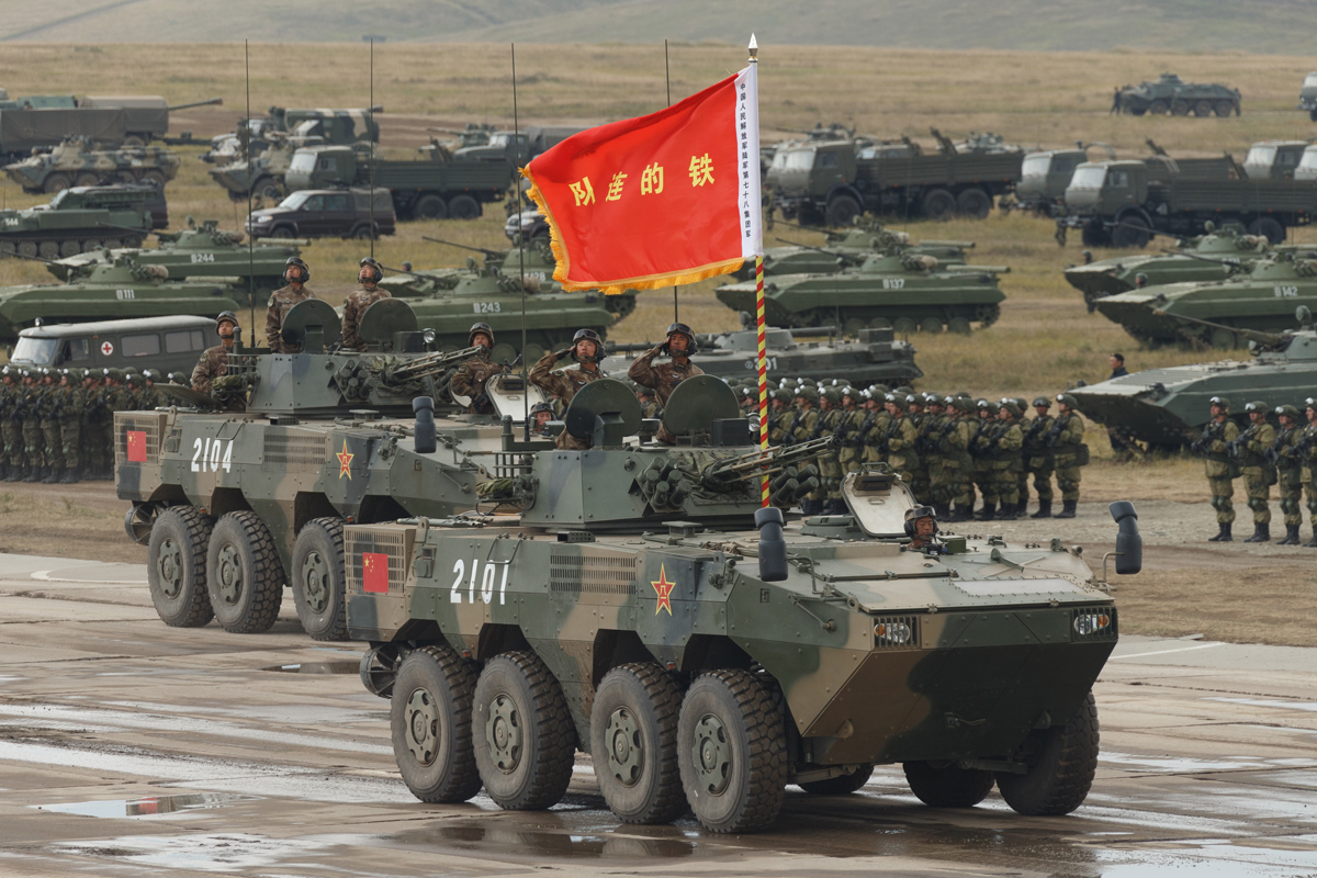 A Chinese People's Liberation Army eight-wheeled infantry fighting vehicle moving along a parade ground in a line, with soldiers marching behind it.