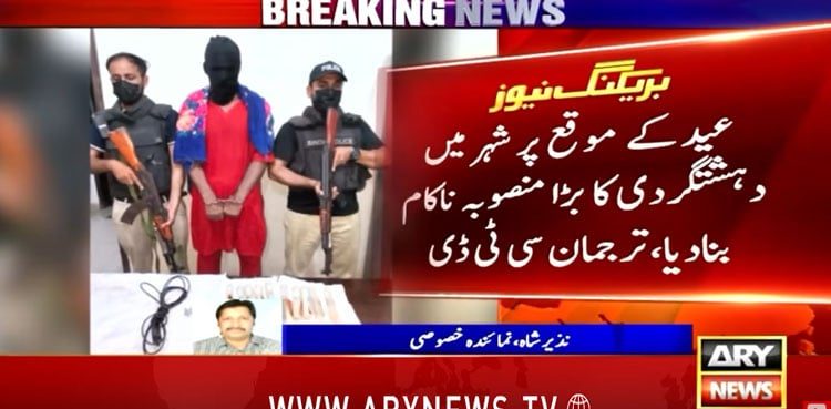 A still from an ARY News broadcast showing a detainee in custody with masked security personnel and recovered wire fuses.