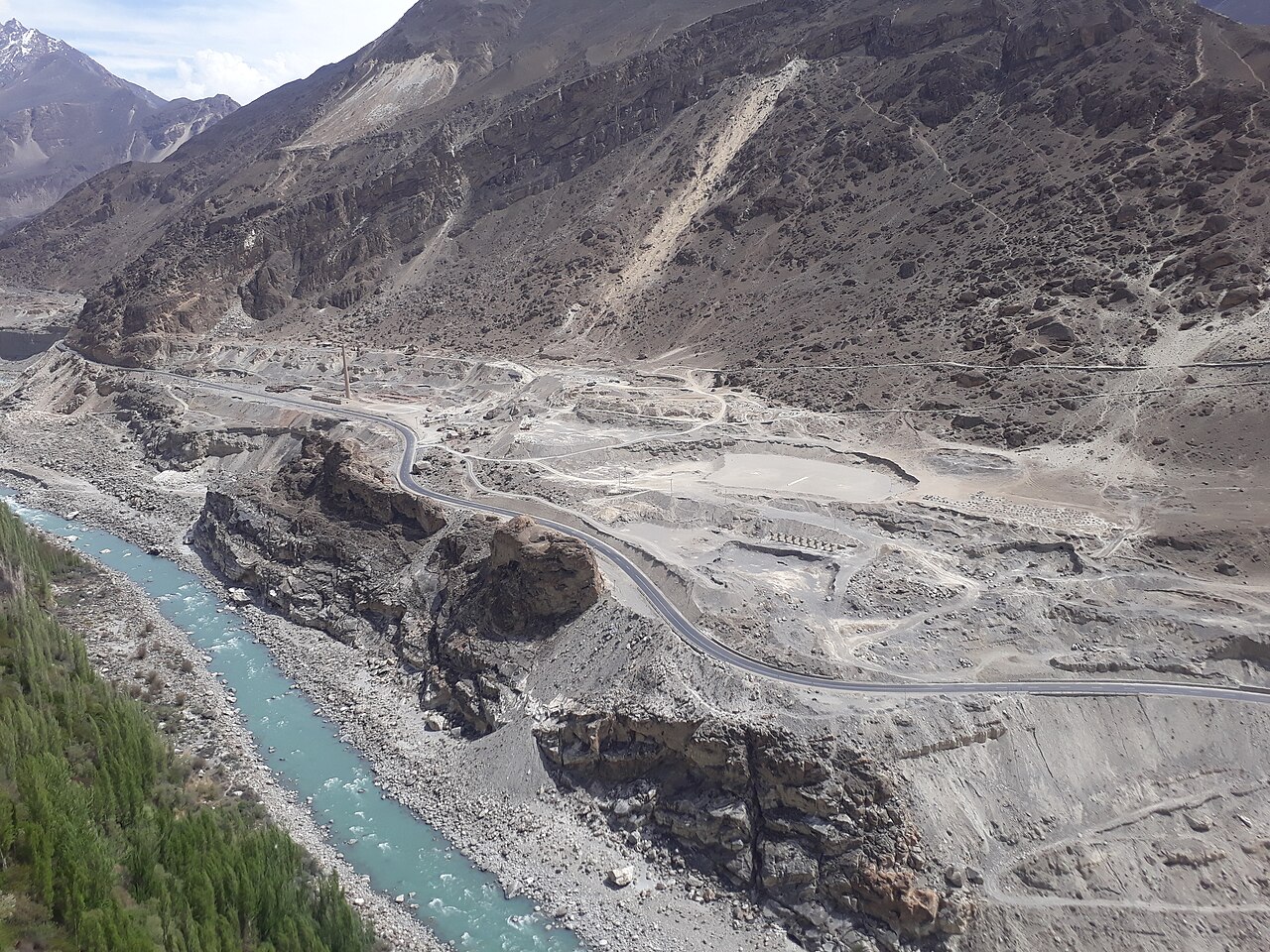 A paved mountain road, the Karakoram Highway, winding between rocky slopes above a river gorge.