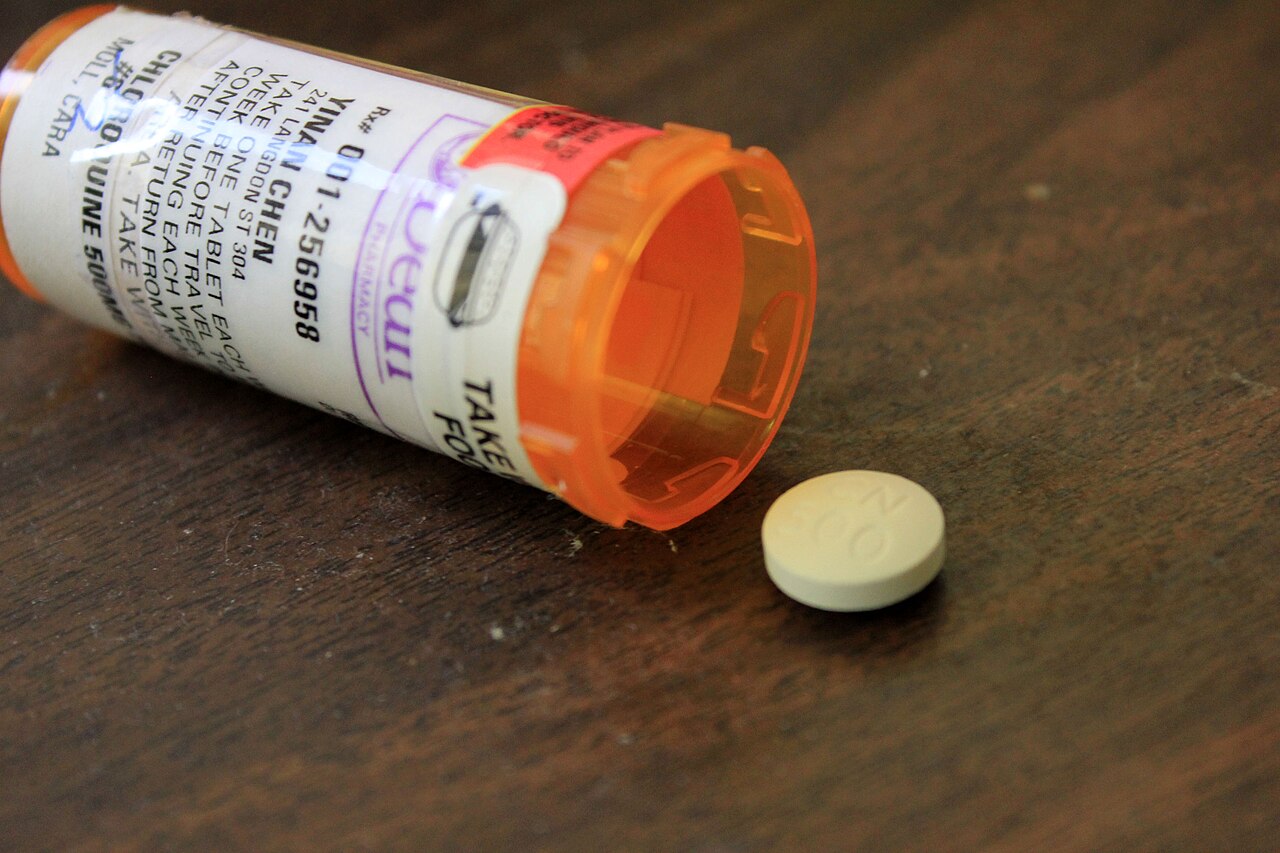 A medicine container and a white tablet on a plain surface.