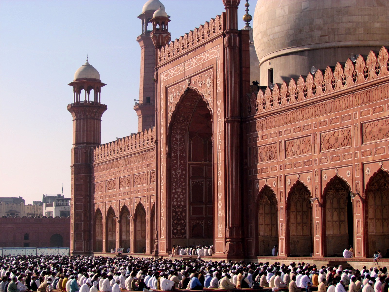 Worshippers gathered for Eid prayers in the courtyard of the Badshahi Mosque in Lahore, its red sandstone facade and minarets visible behind them.