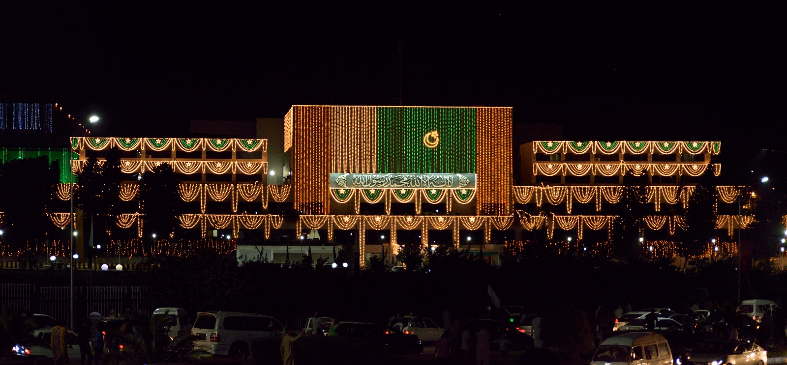 The illuminated Parliament House of Pakistan at night in Islamabad, with its dome and minaret silhouettes against a deep blue sky.
