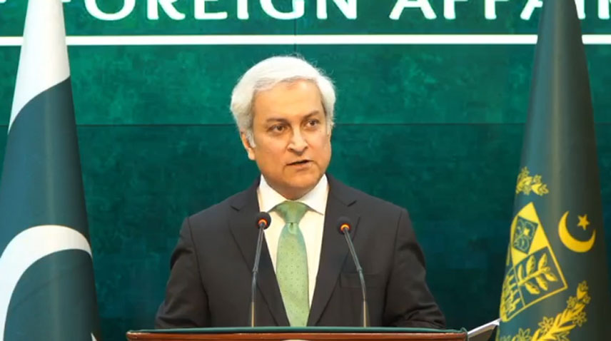 Foreign Office spokesperson Tahir Hussain Andrabi speaking at a podium with Pakistan flags.