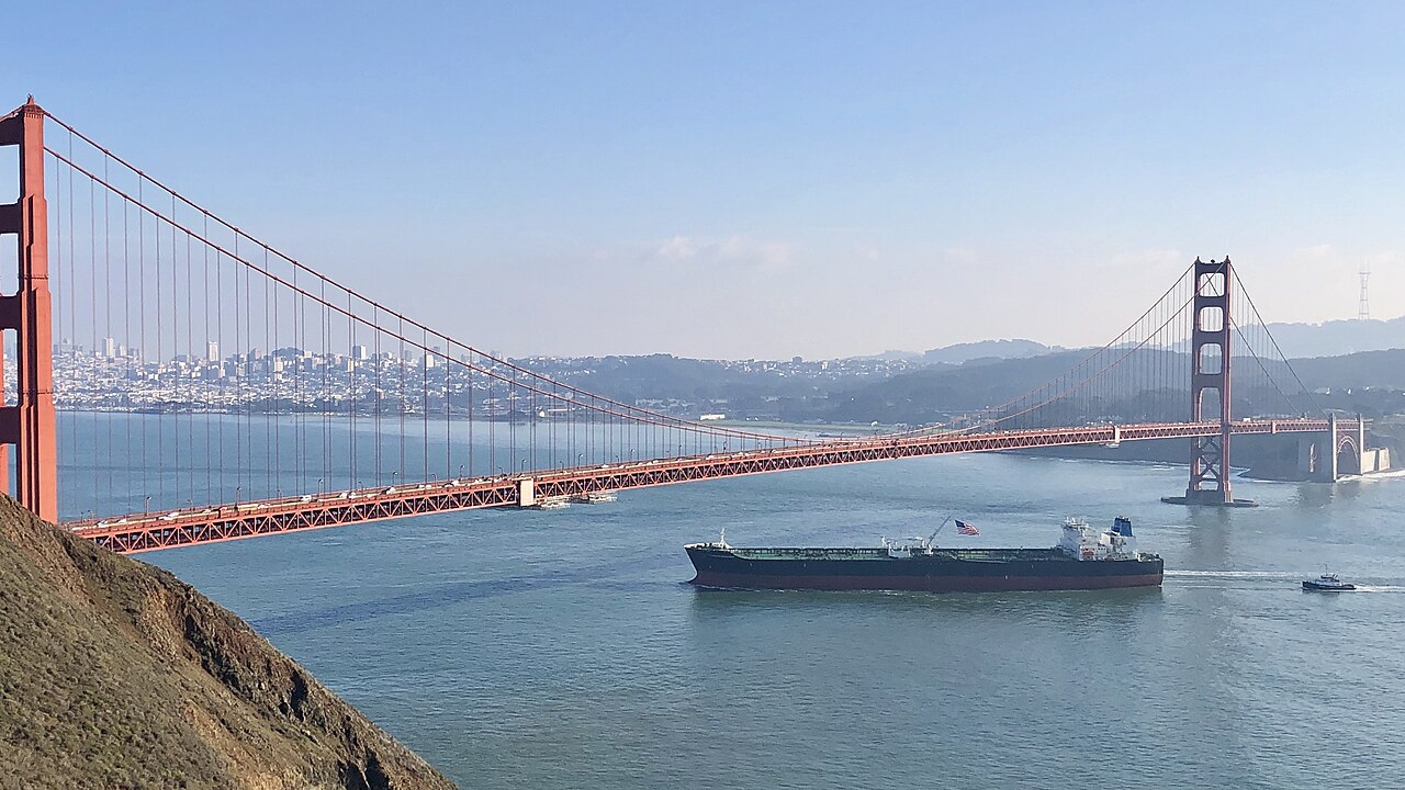 A large commercial oil tanker passes under the Golden Gate Bridge in daylight