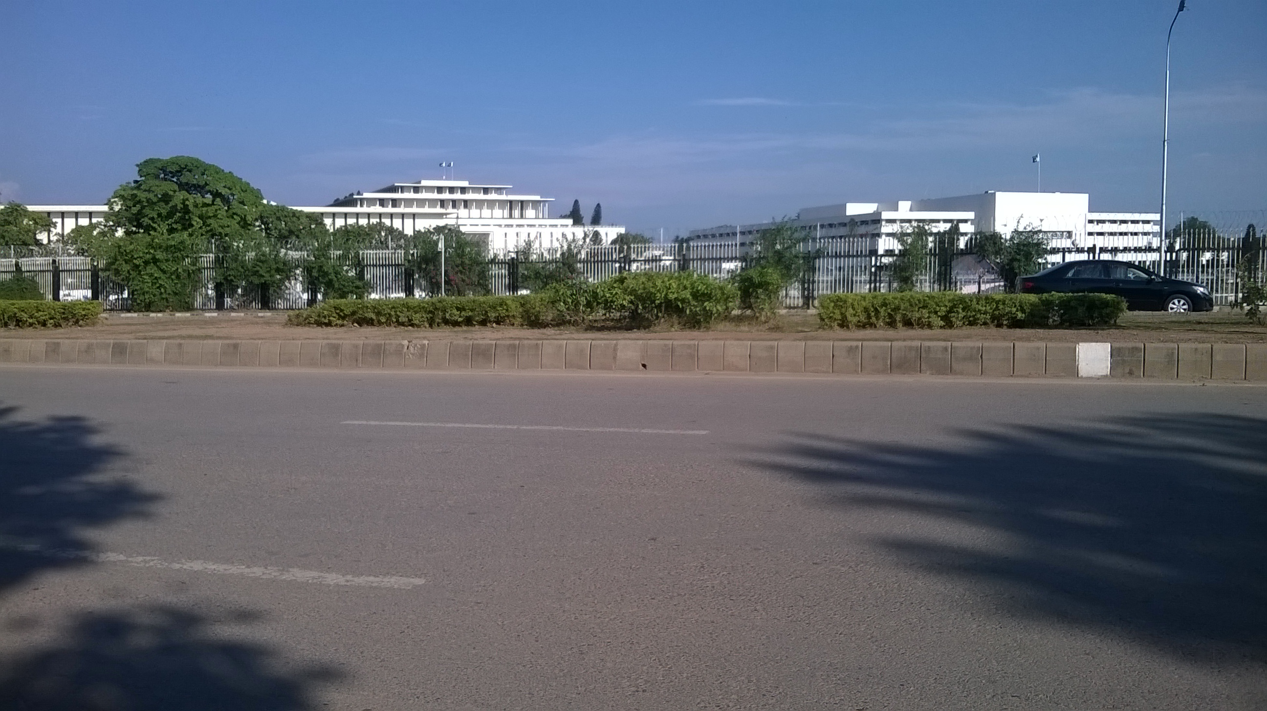Daytime view of Pakistan's Parliament House and the adjacent President House in Islamabad, seen across lawns and a roadway.