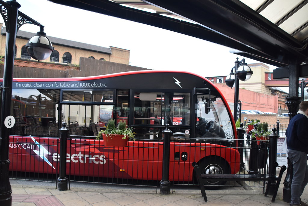 An electric bus parked at a UK bus station, painted in pale blue and white, photographed from the kerb side with the destination display above the windscreen.