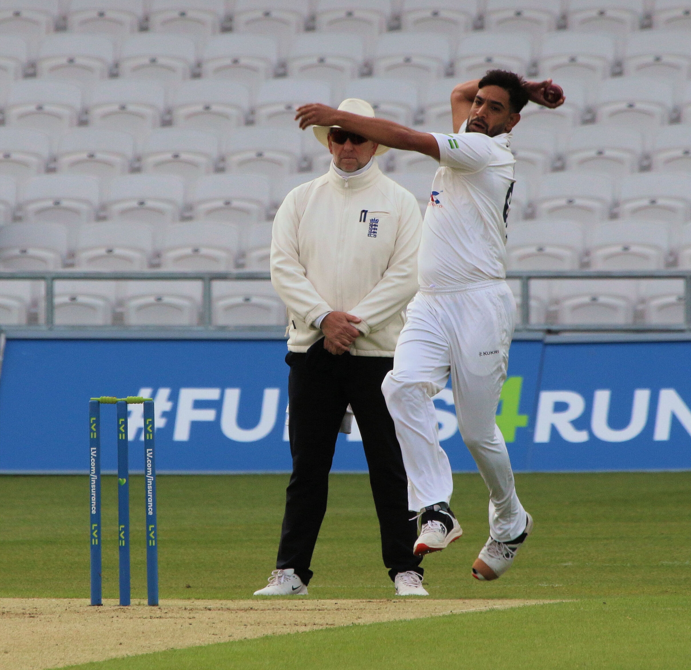 Haris Rauf in his bowling stride, right arm high in delivery, with the stumps and an umpire in white behind him.