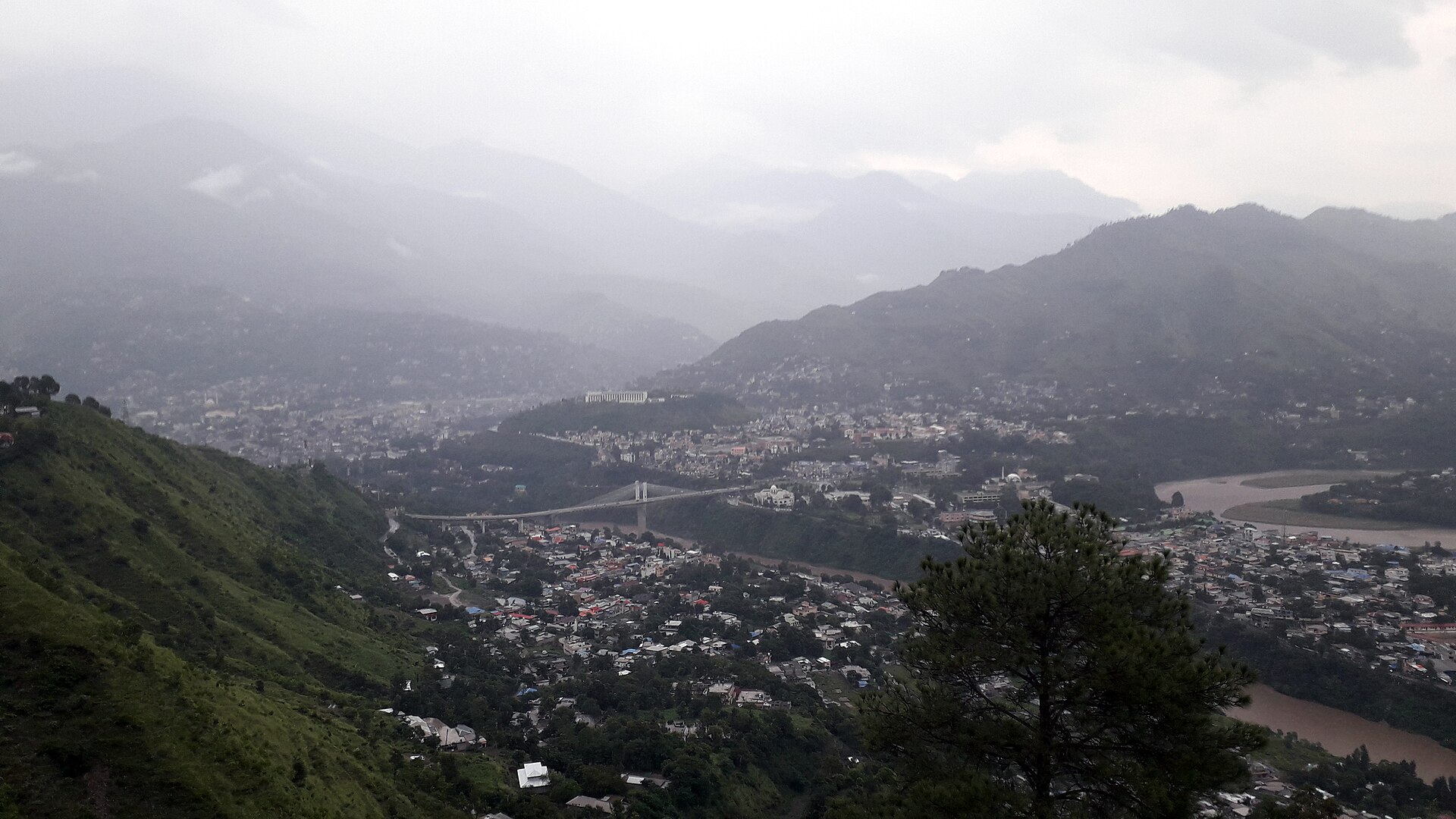 A hillside city of densely packed buildings spread along a river valley in Azad Jammu and Kashmir.