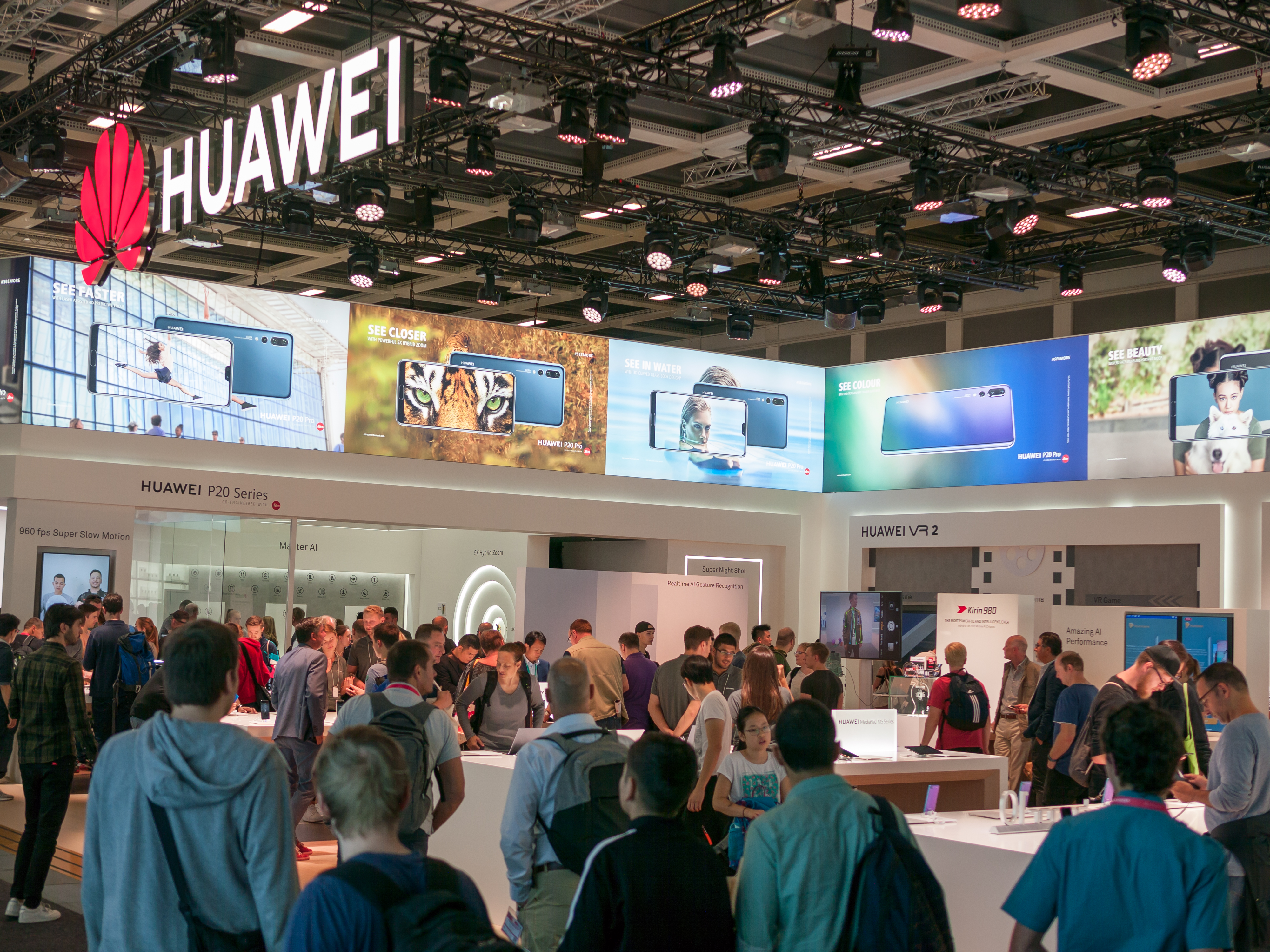A brightly lit Huawei exhibition booth at the IFA 2018 trade show in Berlin, with the company name on a large display and visitors visible behind a barrier