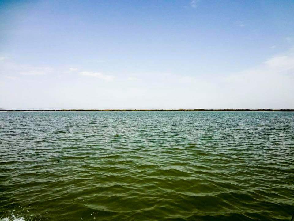 A wide view of the Chashma Barrage reservoir in Mianwali, Pakistan, with water and low hills under a hazy sky