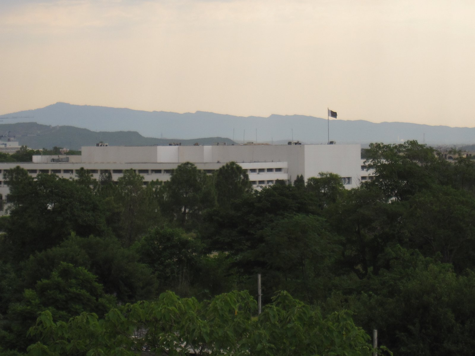 The Parliament House building in Islamabad seen from across its lawns, with the main hall and colonnaded wings in daylight