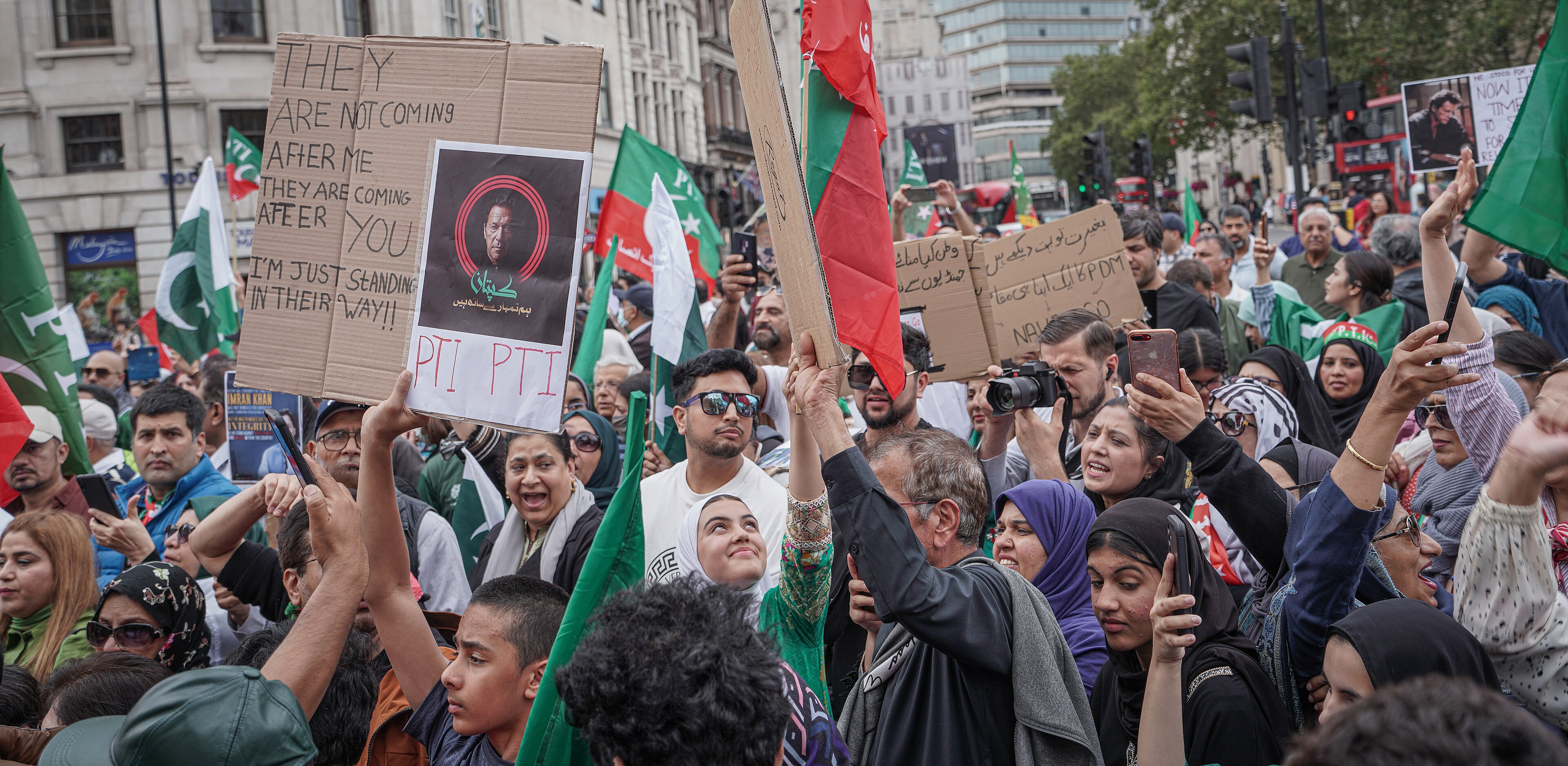 A crowd of demonstrators gathered at the edge of Trafalgar Square in London, some holding flags and banners