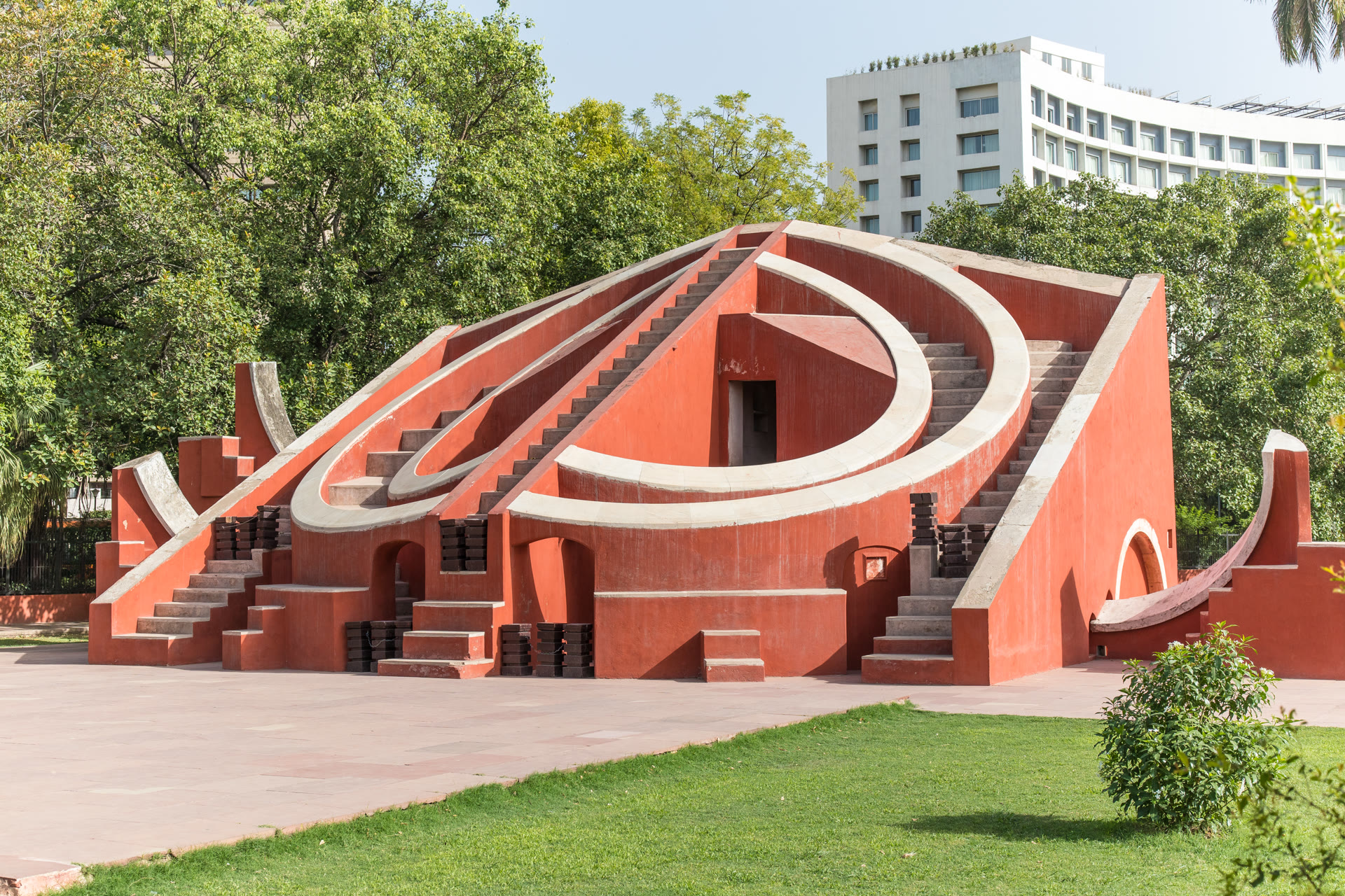 A wide view of the red stone astronomical instruments of Jantar Mantar in New Delhi under a clear blue sky.