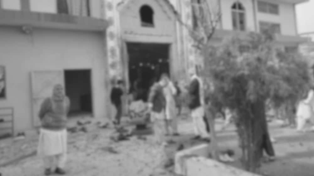 A grainy photograph of debris-strewn ground and people standing outside the entrance of a building after an explosion.