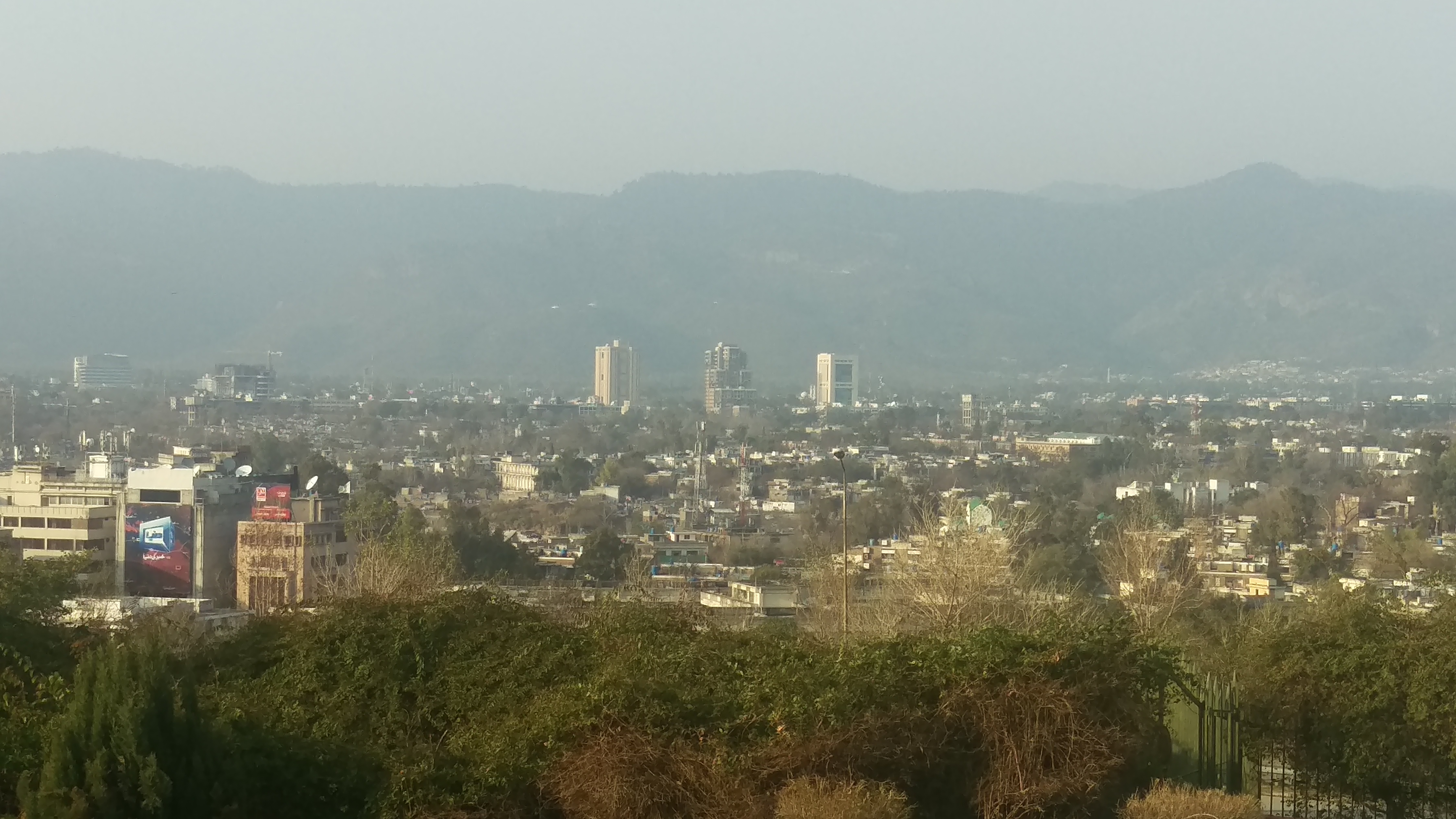 Wide view of the Islamabad skyline seen from the Pakistan Monument, with the city's tree-lined sectors and the Margalla Hills under daylight.