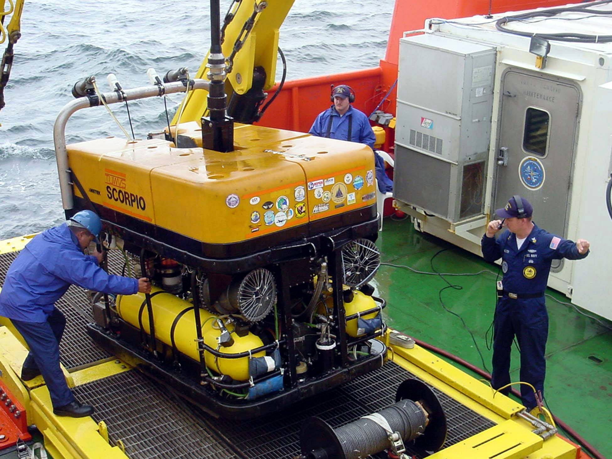 A remotely operated submersible being recovered to a support vessel by a crew member in working gear.