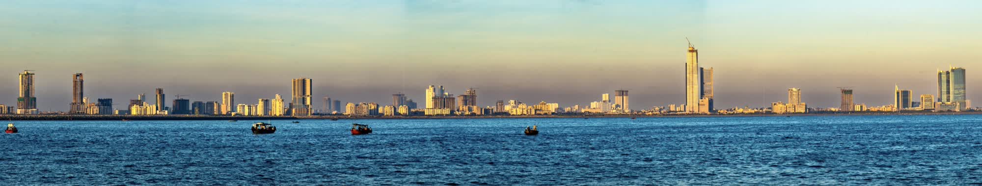 Karachi skyline seen from the Arabian Sea, a thin band of high-rise buildings along a wide coastline under a pale sky