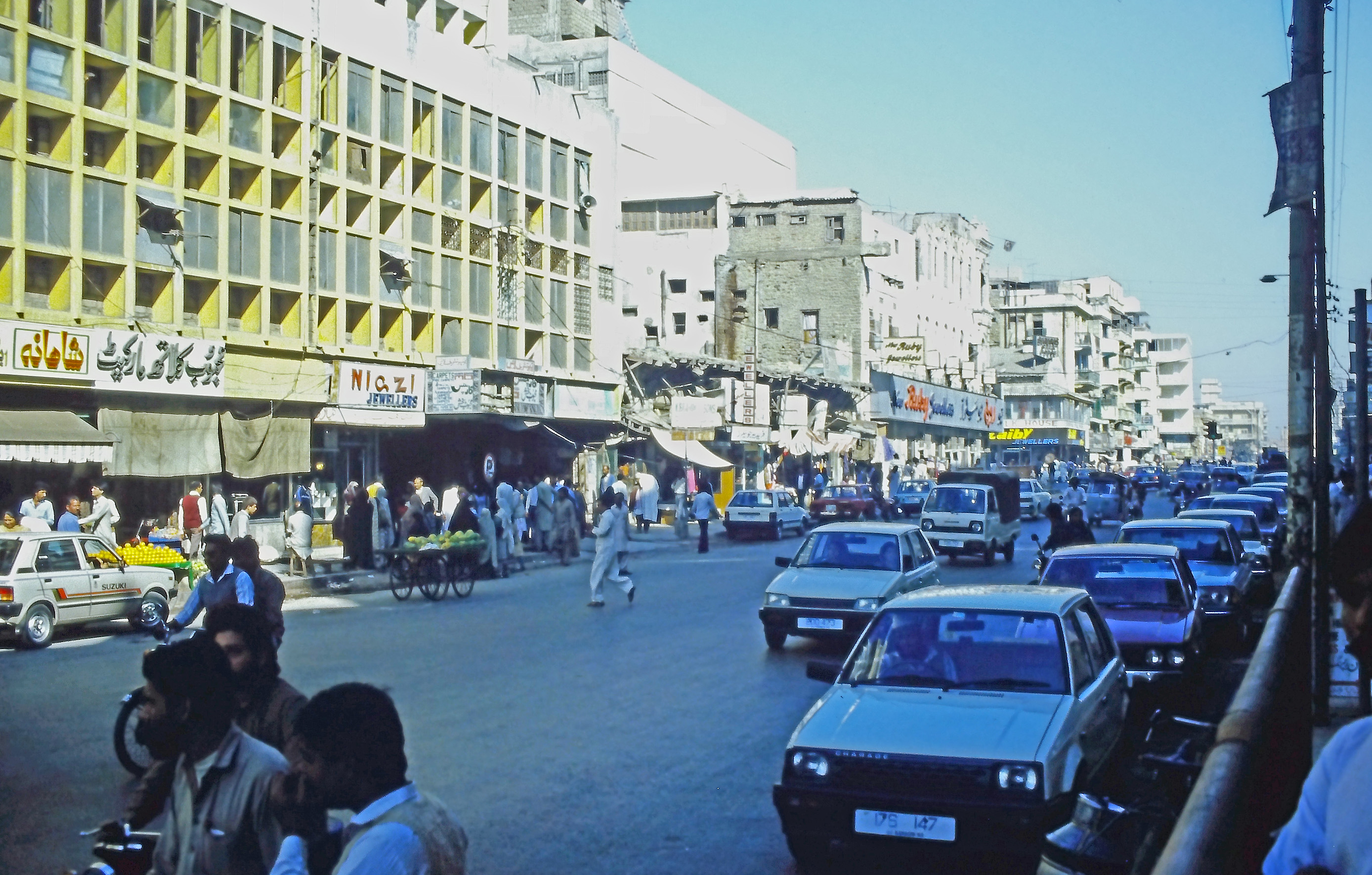A pedestrian street scene in Karachi, Pakistan, with low-rise buildings and overhead wiring.