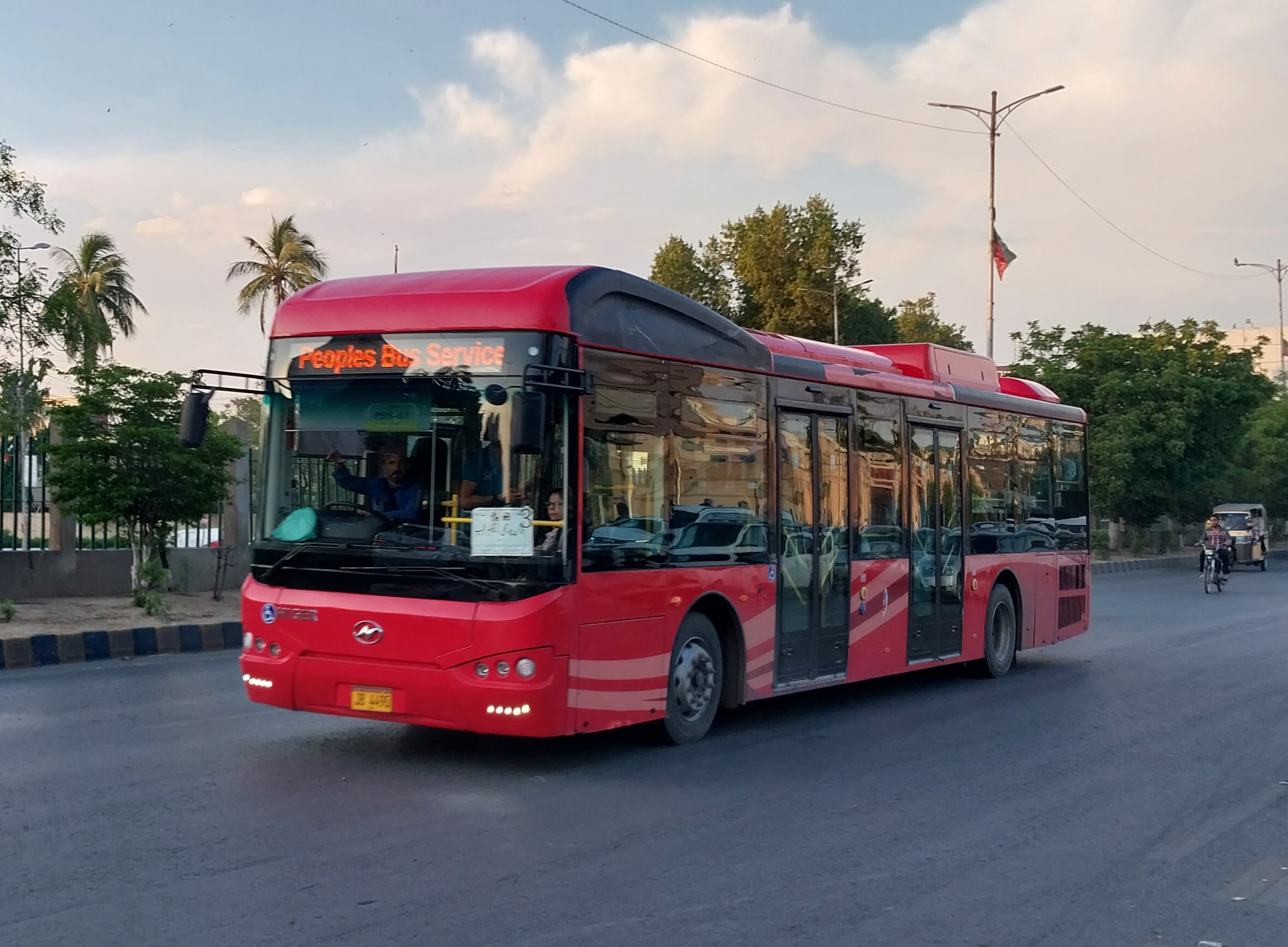 A red People's Bus Service bus on a road in Karachi.