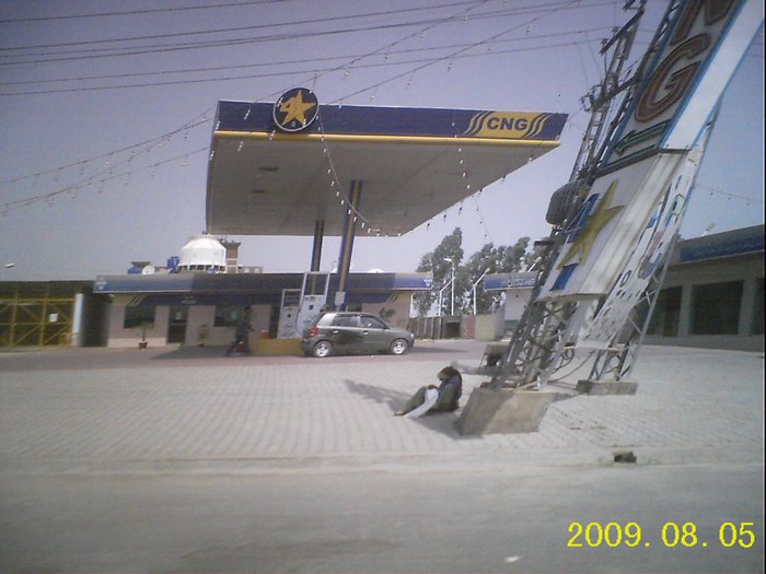 A car being refuelled at a compressed natural gas station in Pakistan, with a dispenser and canopy visible.