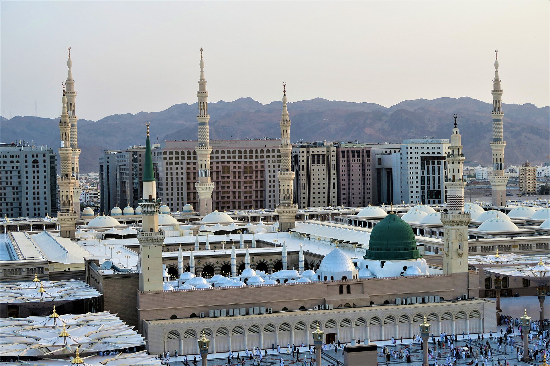 Aerial view of the Prophet's Mosque in Madinah, showing its white roofs, minarets and surrounding plaza.
