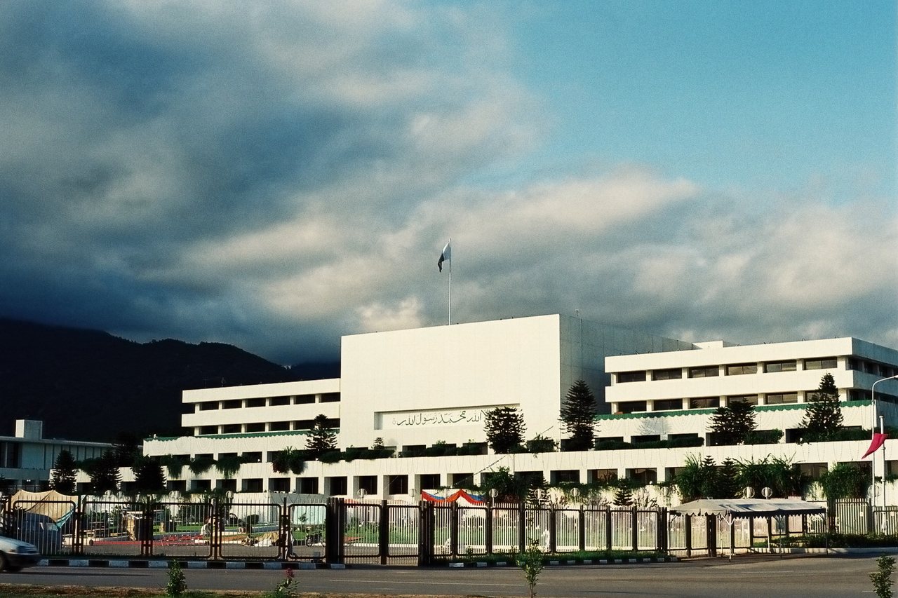 The white, tent-like Parliament House building in Islamabad with its sloping roof and surrounding trees.