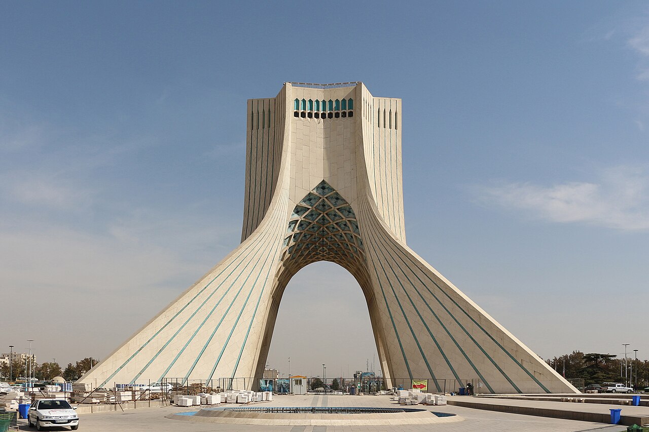 The Azadi Tower in Tehran, Iran, rising above a landscaped plaza under a clear blue sky.