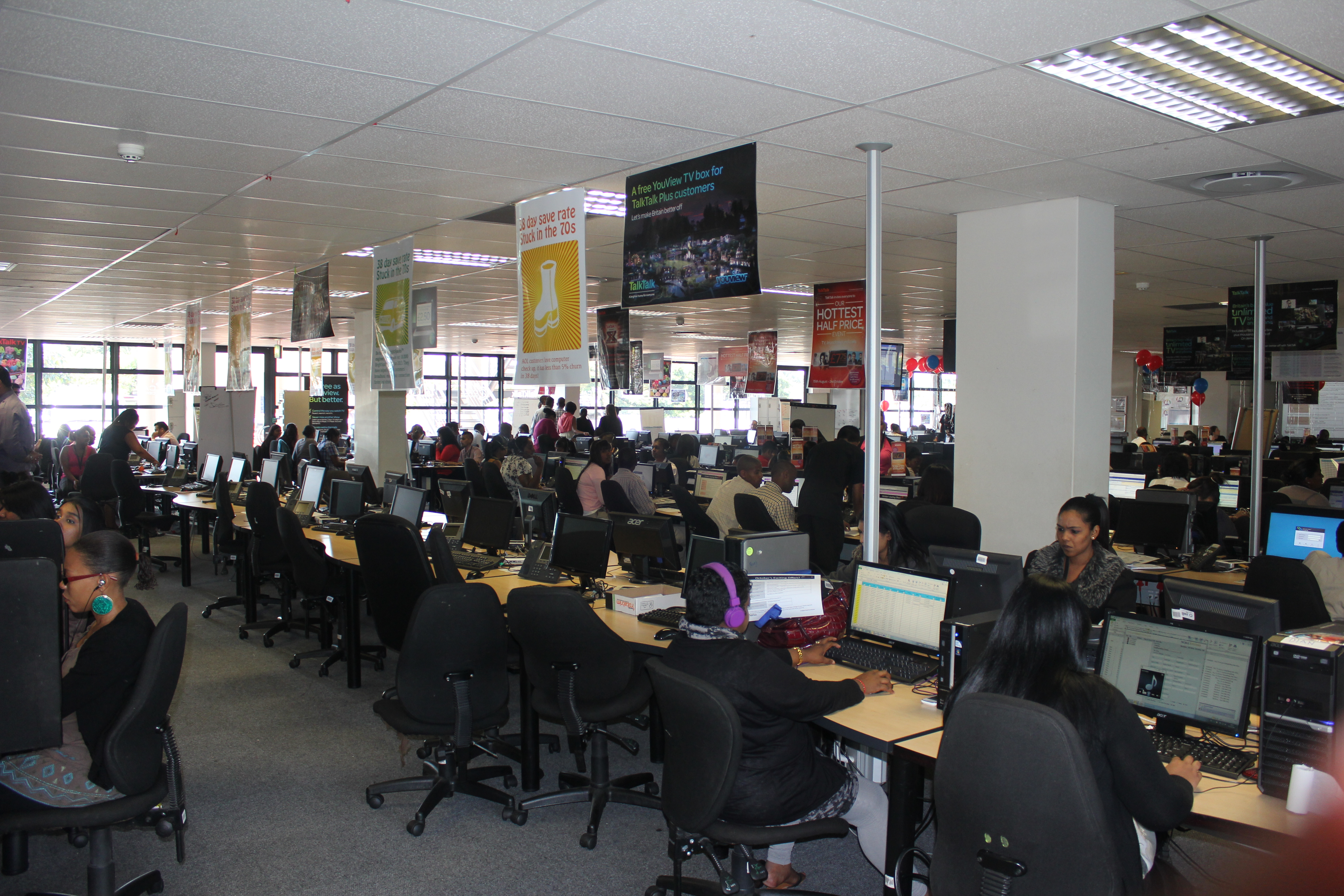 A row of workstations in a call centre, with employees seated at computers wearing headsets