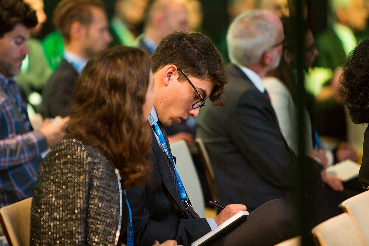 Attendees at a cyber security conference, with a speaker addressing an audience in a conference hall