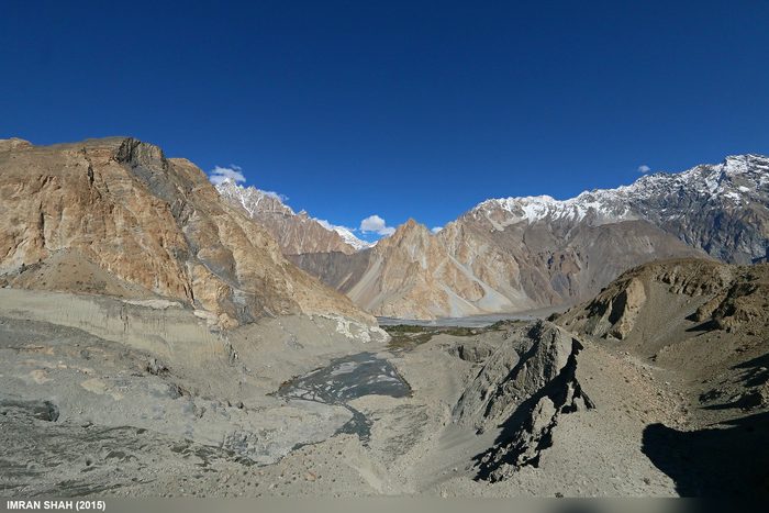 The Passu Glacier and surrounding rugged mountains in Gilgit-Baltistan, with a braided glacial river bed in the foreground and snow-capped peaks on the horizon.