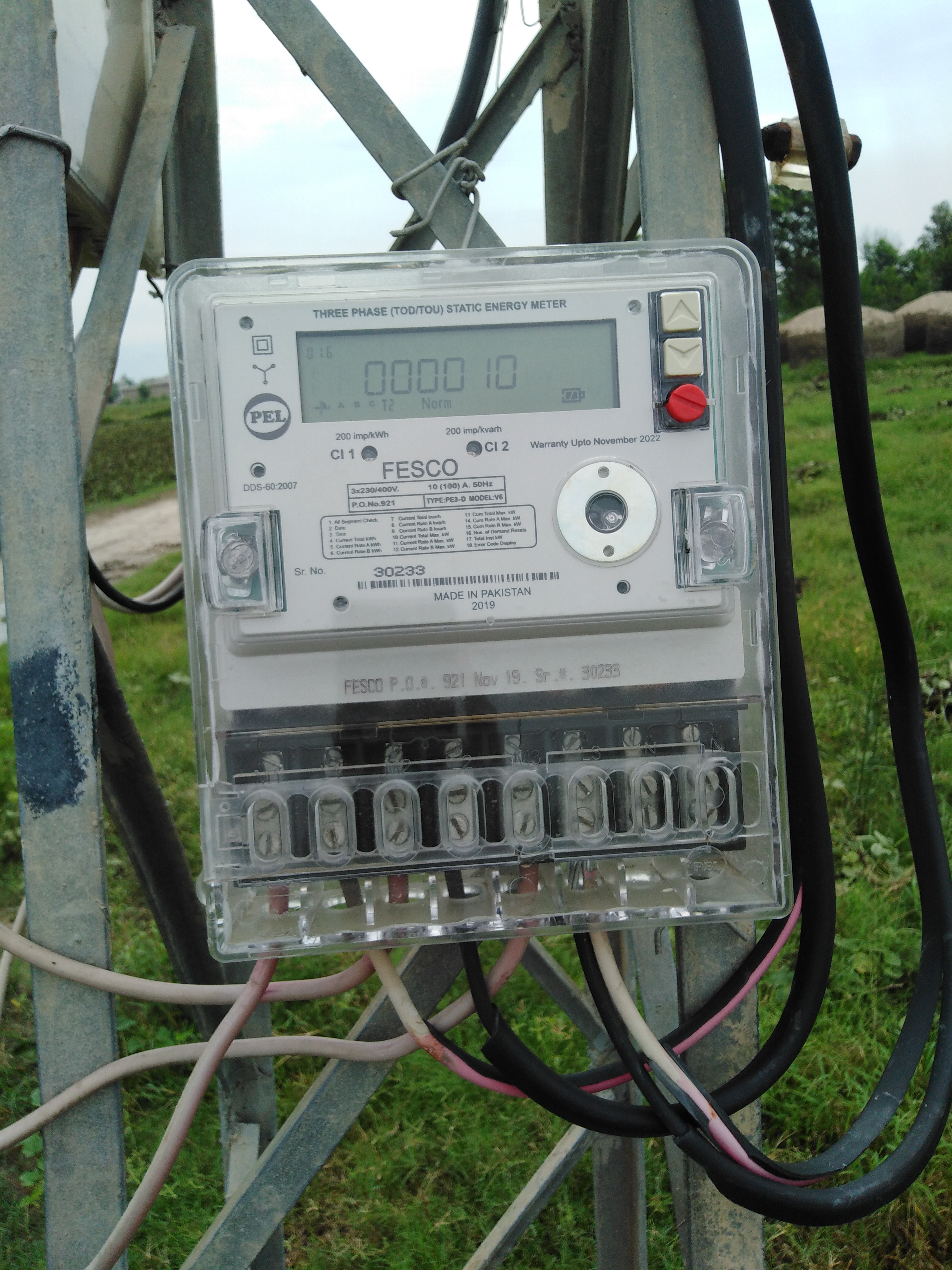 A three-phase digital electricity meter mounted on a metal pole, with its screen showing a reading of 0000 10 and its body marked FESCO and made in Pakistan.