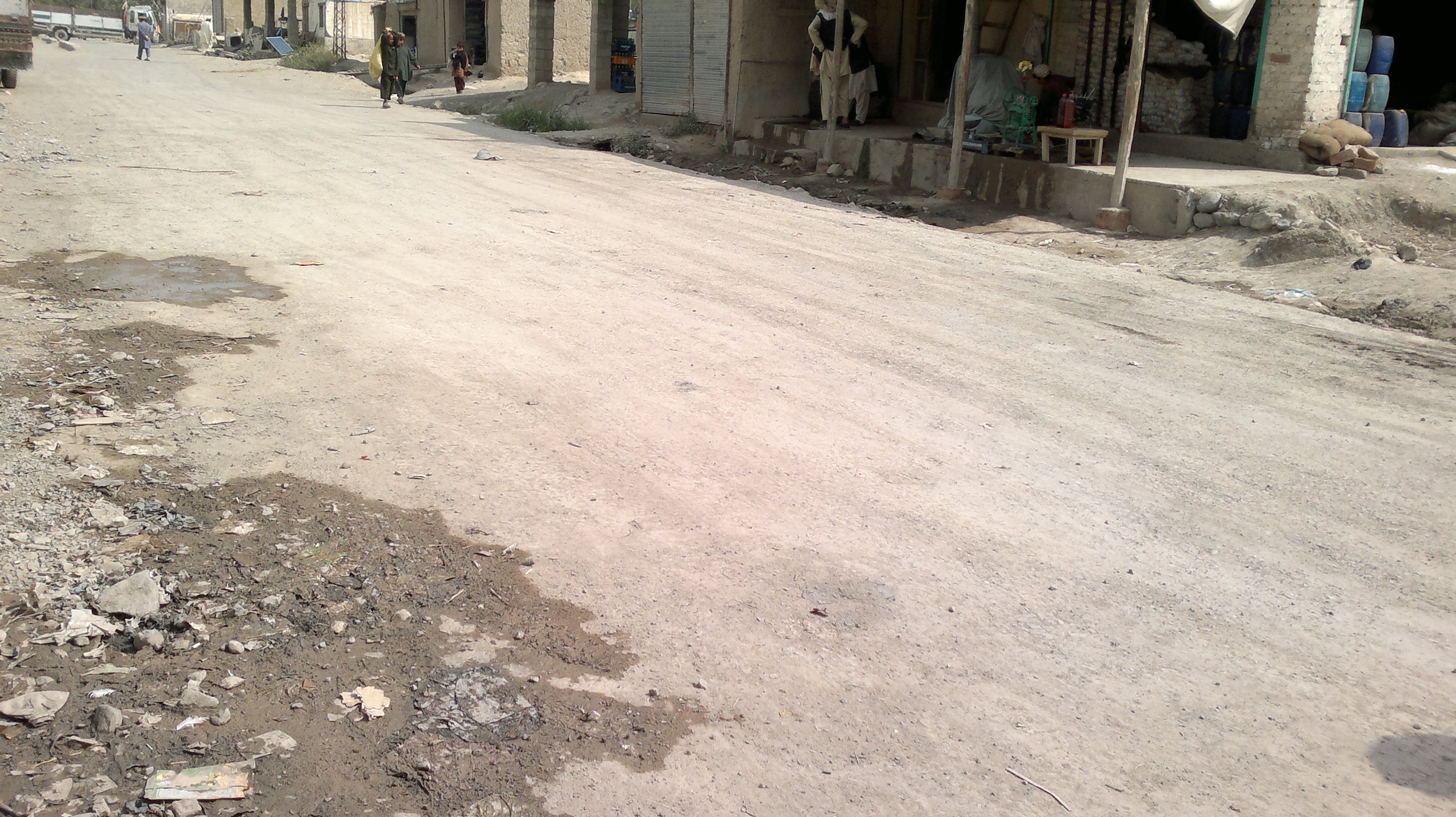 A mostly empty street lined with low shops in Digan, North Waziristan, with a few people walking in the distance.