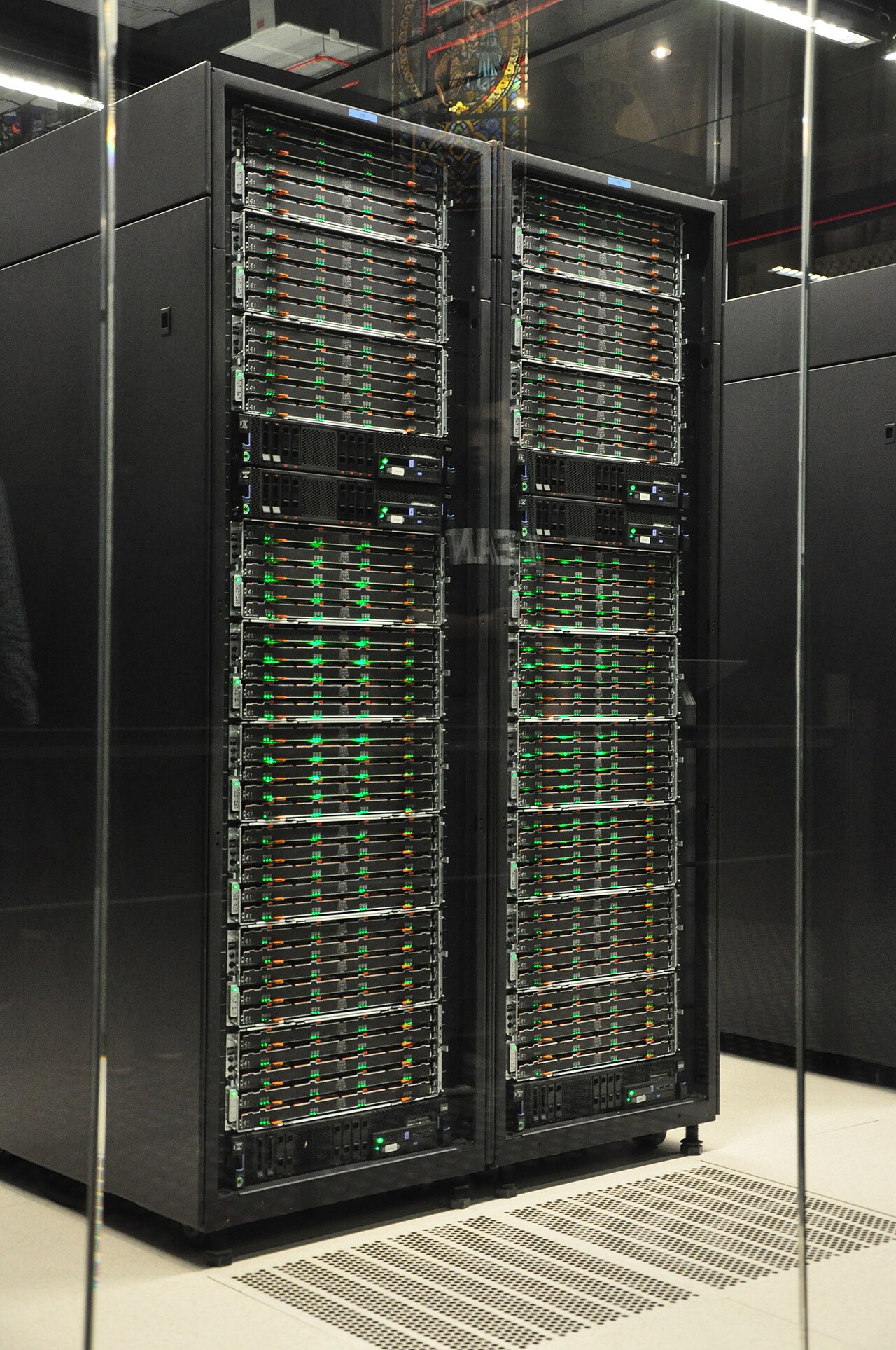 Rows of black server racks in the MareNostrum 4 supercomputer hall at the Barcelona Supercomputing Centre, with status lights glowing along the equipment
