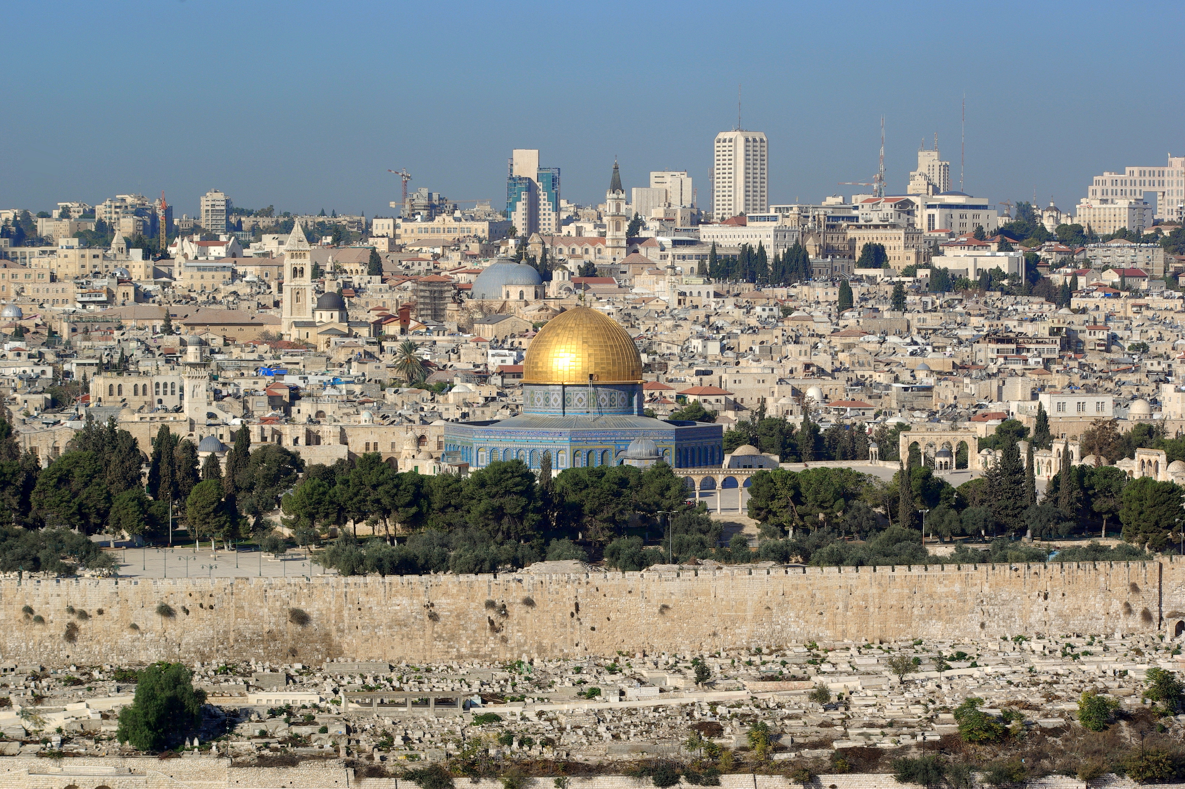 The gold-capped Dome of the Rock and surrounding stone buildings in Jerusalem's Old City, seen from a distance under a clear sky.