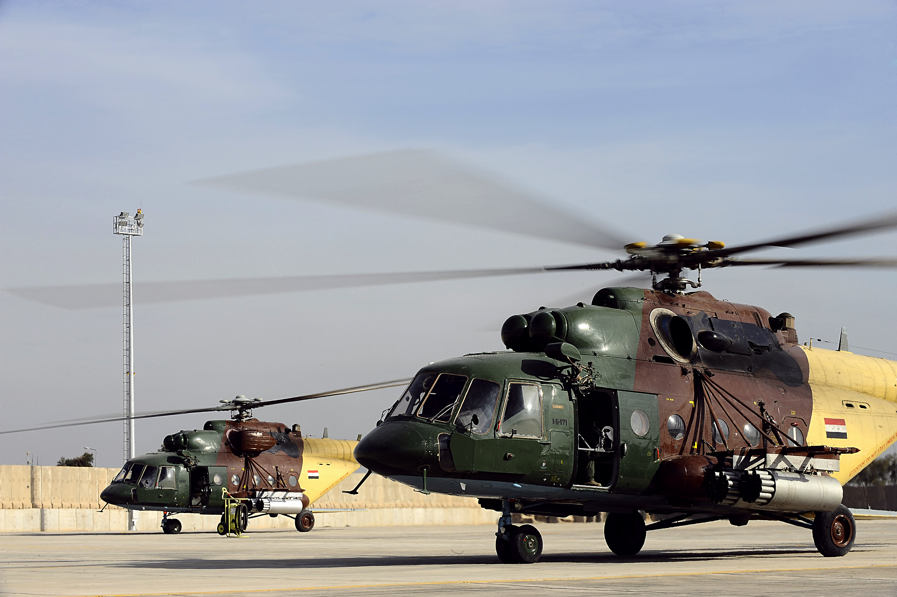 Two Mil Mi-17 transport helicopters parked on an airfield apron with their rotor blades visible.