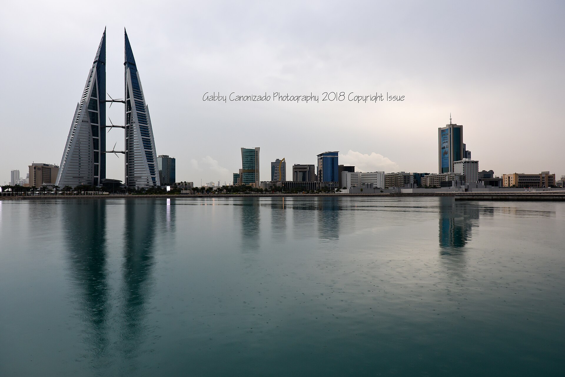 The twin sail-shaped towers of the Bahrain World Trade Center, photographed against an overcast morning sky in Manama.