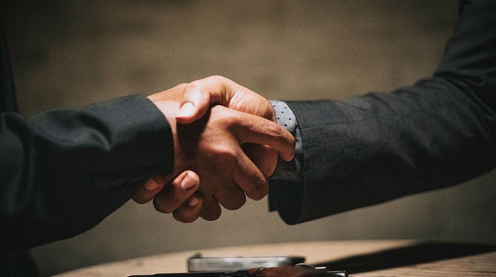 Two people in business suits shaking hands over a desk