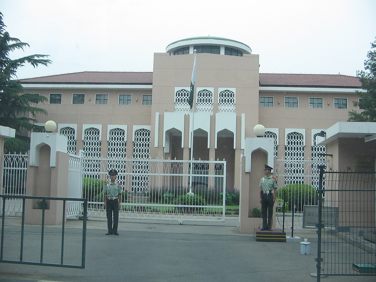 Exterior view of the Embassy of Pakistan in Beijing, with the Pakistani flag visible at the entrance and a wide street in the foreground.