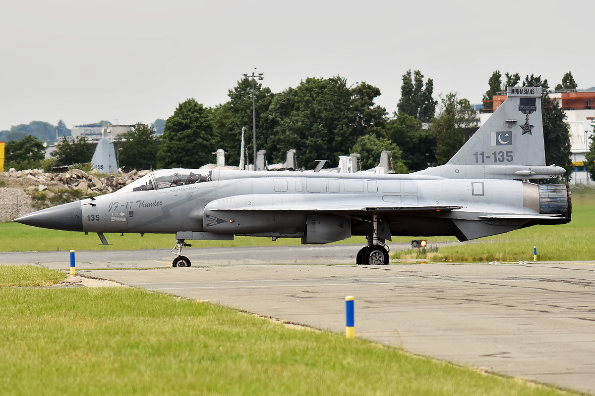 A Pakistan Air Force JF-17 Thunder fighter jet parked on a tarmac, seen from the front-left with its canopy open and a green-and-white tail flash.