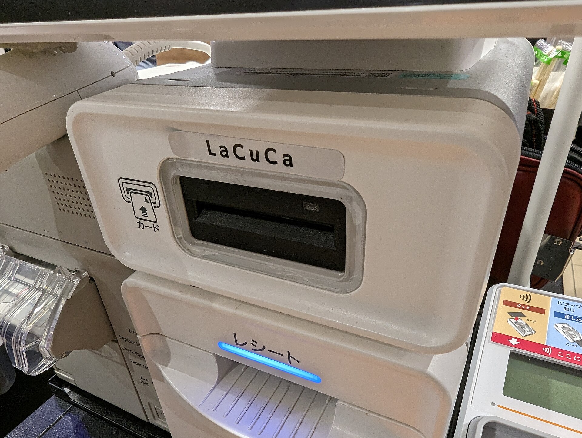 A handheld card payment terminal at a supermarket checkout, with a payment card inserted and a small screen and numeric keypad visible.