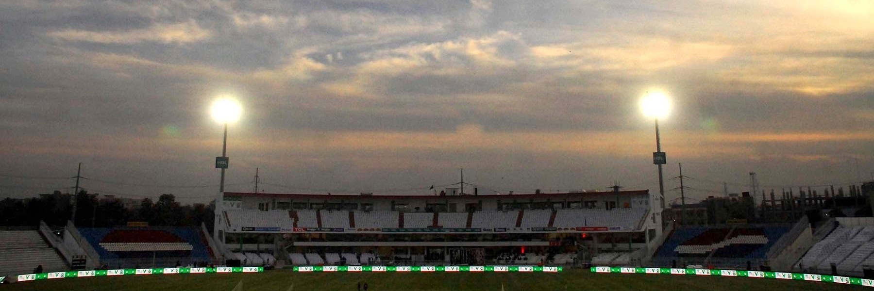 Floodlights above the stands at Rawalpindi Cricket Stadium at dusk, with the outfield and advertising boards visible in the foreground.