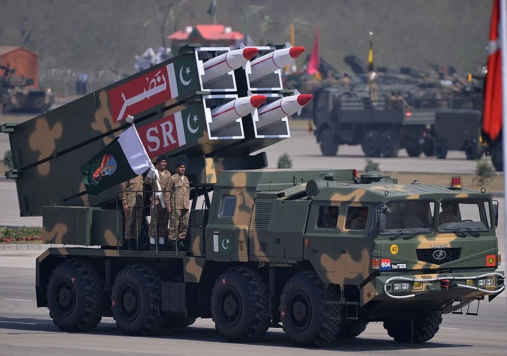 A Pakistani Army missile launcher carrying four white-tipped missiles elevated on a camouflaged truck during a military parade, with soldiers standing on the vehicle.