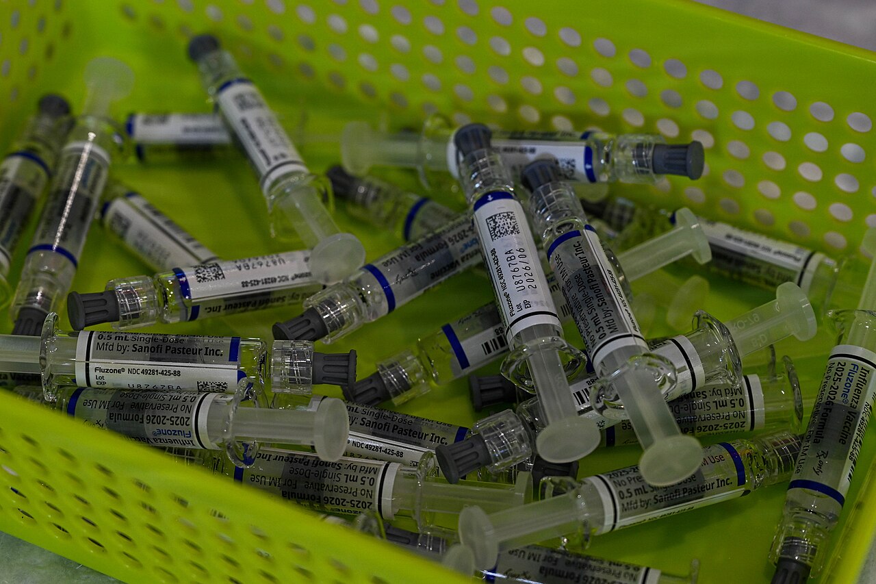 A lime-green plastic crate filled with small glass vaccine vials lying in rows, each carrying a white manufacturer label.