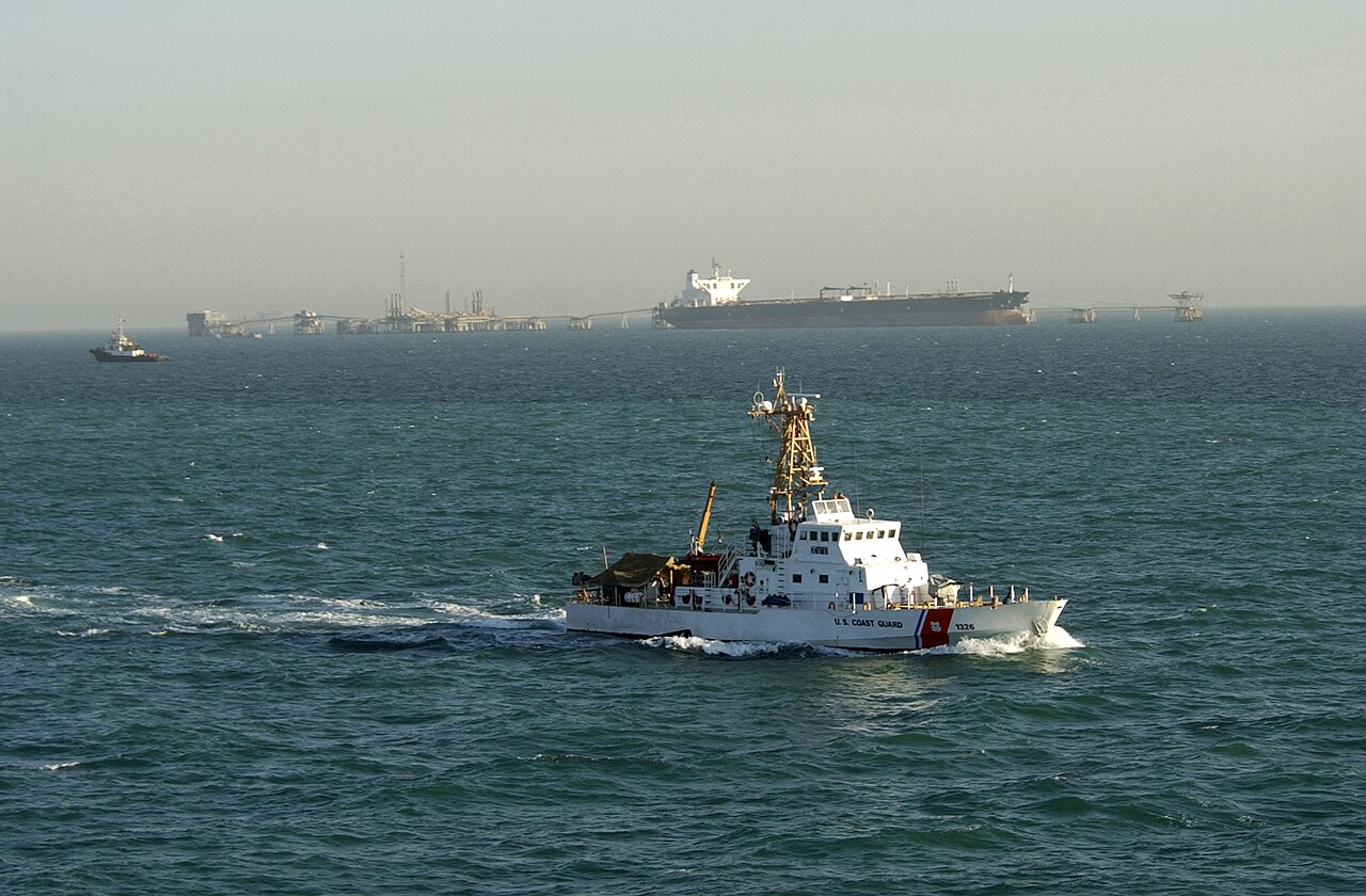 A supertanker taking on crude oil near an offshore terminal in the Persian Gulf, with a smaller patrol vessel alongside.