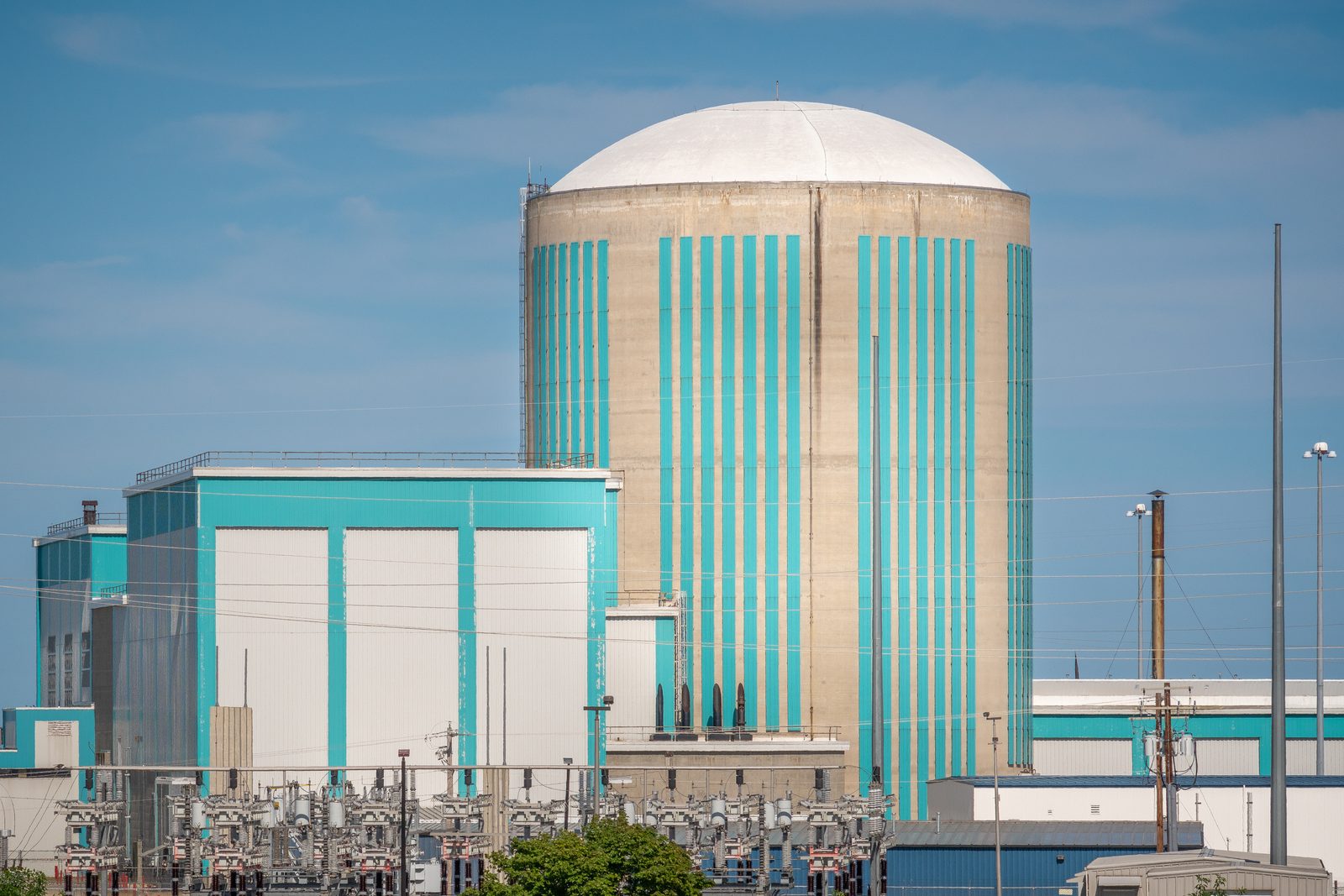A nuclear power station on the shore of a large lake, with a domed containment building, low turbine buildings and steam rising under a clear sky.