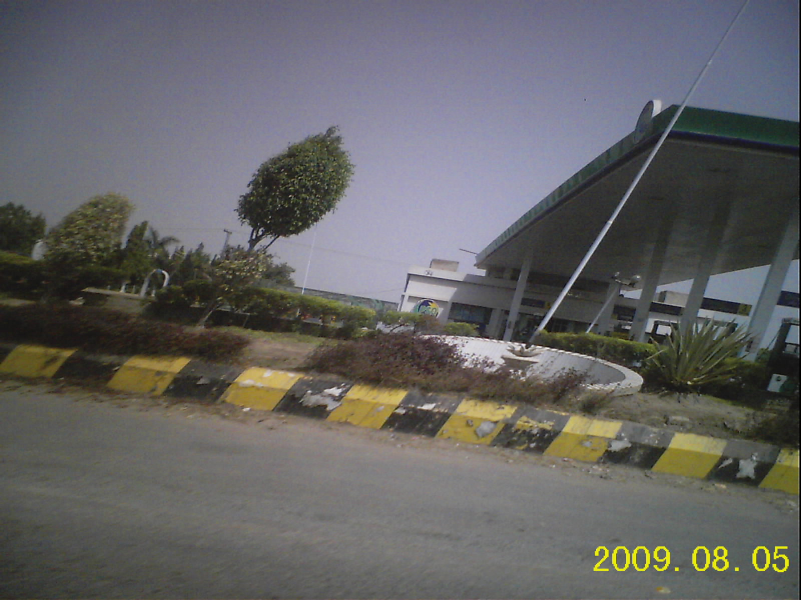 A roadside petrol station with a canopy over fuel pumps, a price board and a vehicle parked alongside.